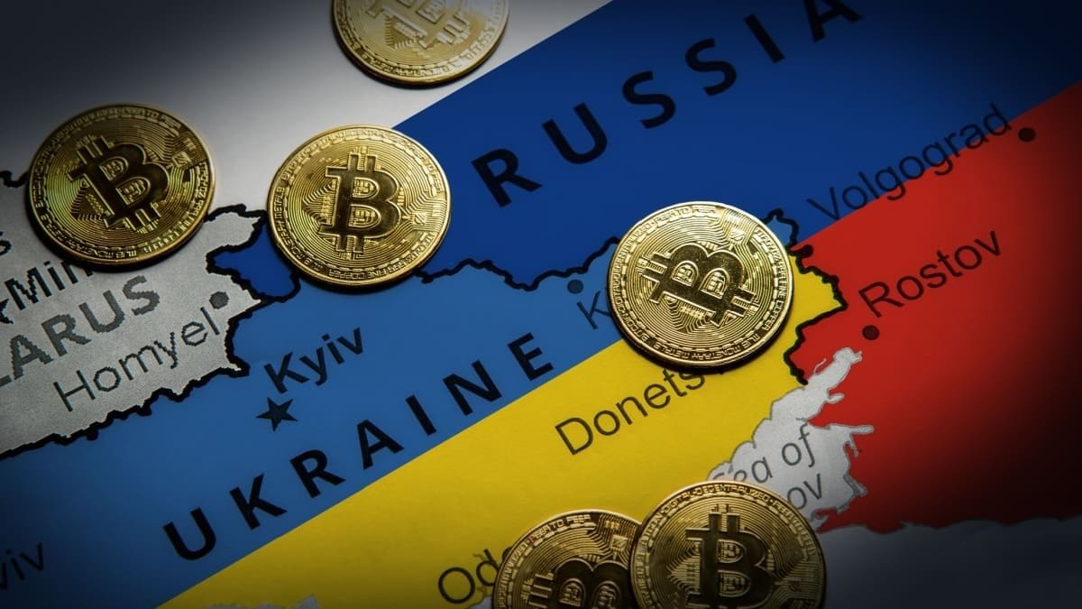 EU sluit achterdeur: cryptoverbod moet Russische oorlogskas raken Een afbeelding van een landkaart met Rusland en Oekraïne, met daartussen bitcoinmunten verspreid
