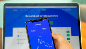 coinbase-2 Telefoon in de voorgrond met de Coinbase Applicatie en op de achtergrond een laptop die de website Coinbase vertoont
