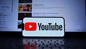 Het logo van Youtube op een mobiele telefoon met op de achtergrond een laptop met het YouTube interface en verschillende video's Het logo van Youtube op een mobiele telefoon met op de achtergrond een laptop met het YouTube interface en verschillende video's
