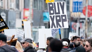 Een afbeelding van een menigte waarvan een aanwezige een bord met 'buy [de crypto] XRP'