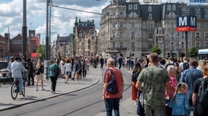 Een afbeelding van een lopende menigte Nederlanders en toeristen in Amsterdam, met een tramrails ertussen Een afbeelding van een lopende menigte Nederlanders en toeristen in Amsterdam, met een tramrails ertussen