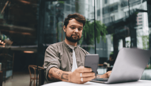Man kijkt naar mobiel achter latop Man kijkt naar mobiel achter latop