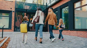 Een afbeelding van een gezin met twee kinderen dat naar een school toe loopt Een afbeelding van een gezin met twee kinderen dat naar een school toe loopt