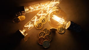 Een afbeelding van bitcoin (BTC) munten tussen een aantal brandende lampen Een afbeelding van bitcoin (BTC) munten tussen een aantal brandende lampen