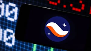 Een afbeelding van het logo van cryptomunt starknet op een mobiele telefoon met op de achtergrond marktdata en grafieken