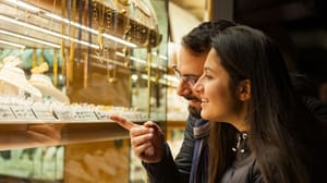Een stel kijkt naar gouden sieraden die zijn belegd met edelstenen bij een juwelier Een stel kijkt naar gouden sieraden die zijn belegd met edelstenen bij een juwelier