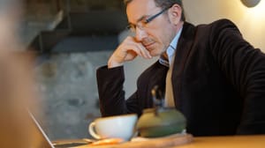 Een afbeelding van een man met een kopje koffie die thuis werkt achter zijn laptop Een afbeelding van een man met een kopje koffie die thuis werkt achter zijn laptop