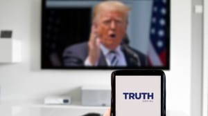 Een afbeelding van donald trump op de achtergrond met op de voorgrond een mobiele telefoon met daarop het logo van sociale mediaplatform truth social Een afbeelding van donald trump op de achtergrond met op de voorgrond een mobiele telefoon met daarop het logo van sociale mediaplatform truth social
