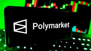 Een afbeelding van het logo van voorspellingsmarkt Polymarket op een mobiele telefoon met een grafiek in de achtergrond Een afbeelding van het logo van voorspellingsmarkt Polymarket op een mobiele telefoon met een grafiek in de achtergrond