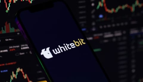 WhiteBIT Coin viert vierde verjaardag met marktwaarde van $16,1 miljard Een afbeelding van whitebit, een cryptomunt afkomstig van een grote crypto exchange. Het logo van whitebit staat op een mobiel, en op de achtergrond staan grafieken