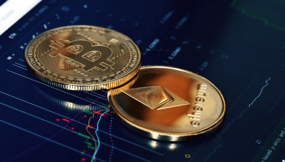 Een digitaal trade scherm met daarop een fysieke Bitcoin en Fysieke Ethereum muntstuk
