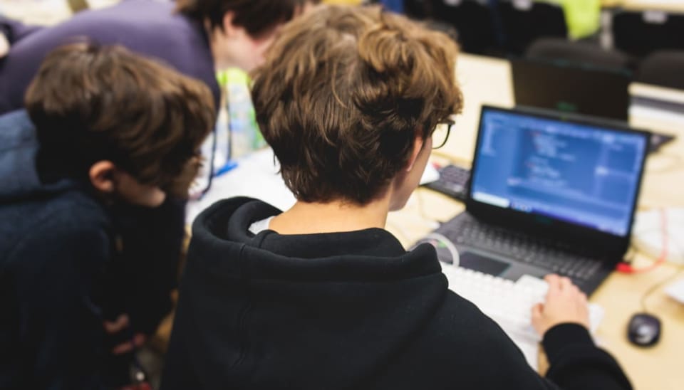 Meerdere studenten werken samen op een laptop aan een hackathon, met software _ code op een laptop