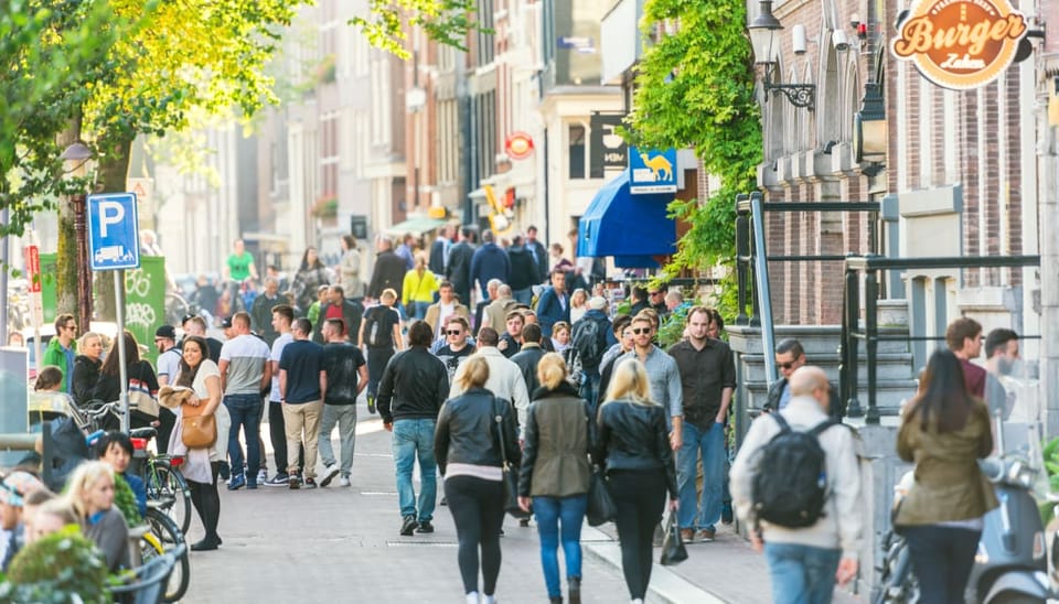 Een afbeelding van Nederlanders en toeristen die lopen door Amsterdam