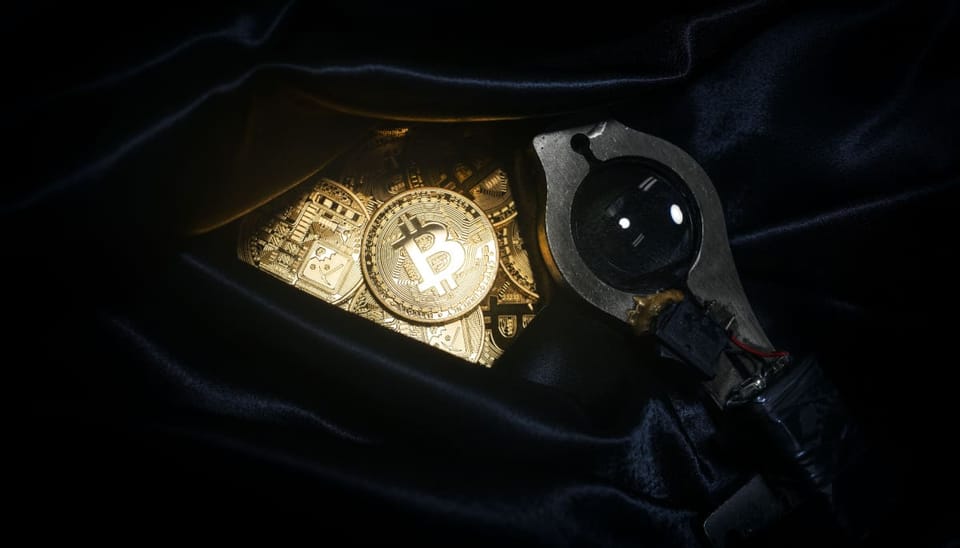 Een afbeelding van bitcoin munten in een weekendtas, vaak gebruikt bij een overval, en een vergrootglas om de zaak te belichten