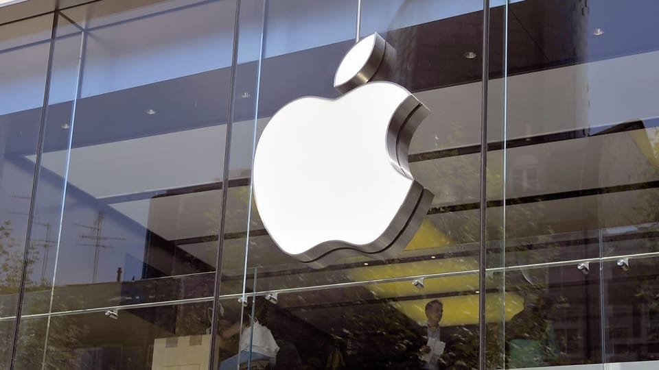 Een afbeelding van het Apple logo op een kantoor, met werkende mensen op de achtergrond