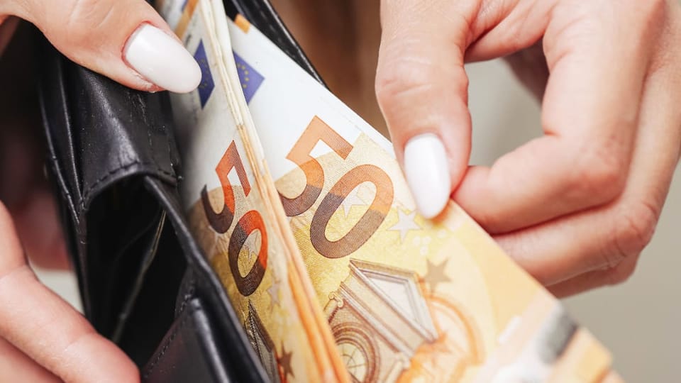 Een afbeelding van vrouwelijke handen die briefjes van 50 euro uit een portemonnee trekken