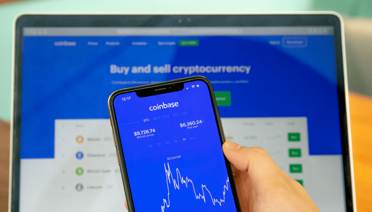 Telefoon in de voorgrond met de Coinbase Applicatie en op de achtergrond een laptop die de website Coinbase vertoont