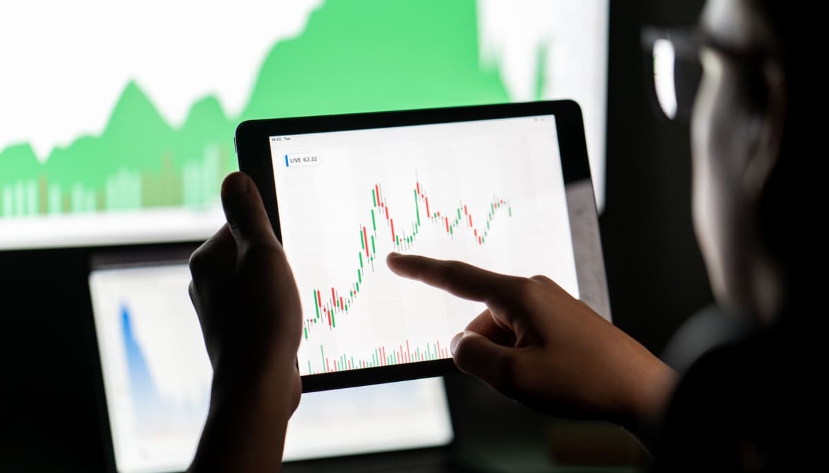 Een foto van een oudere man met een bril die grafieken van crypto analyseert op verschillende beeldschermen