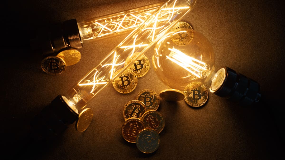 Een afbeelding van bitcoin (BTC) munten tussen een aantal brandende lampen Een afbeelding van bitcoin (BTC) munten tussen een aantal brandende lampen