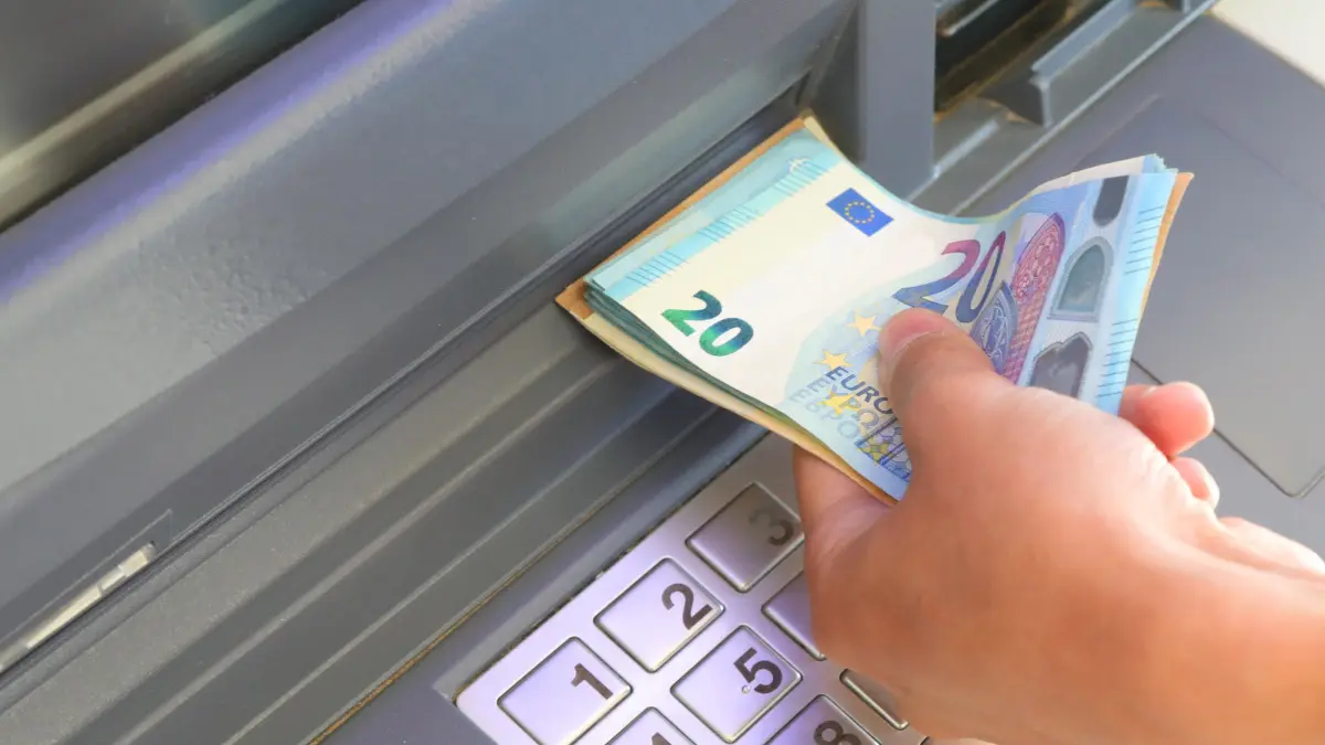 Een afbeelding van iemand die euro bankbiljetten uit een pinautomaat trekt Een afbeelding van iemand die euro bankbiljetten uit een pinautomaat trekt